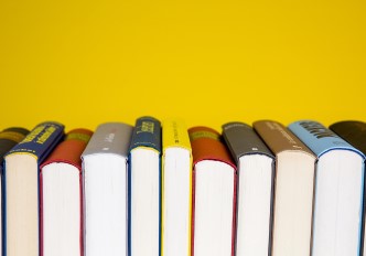 fotografia de livros alinhados com as lombadas na horizontal, sobre um fundo amarelo