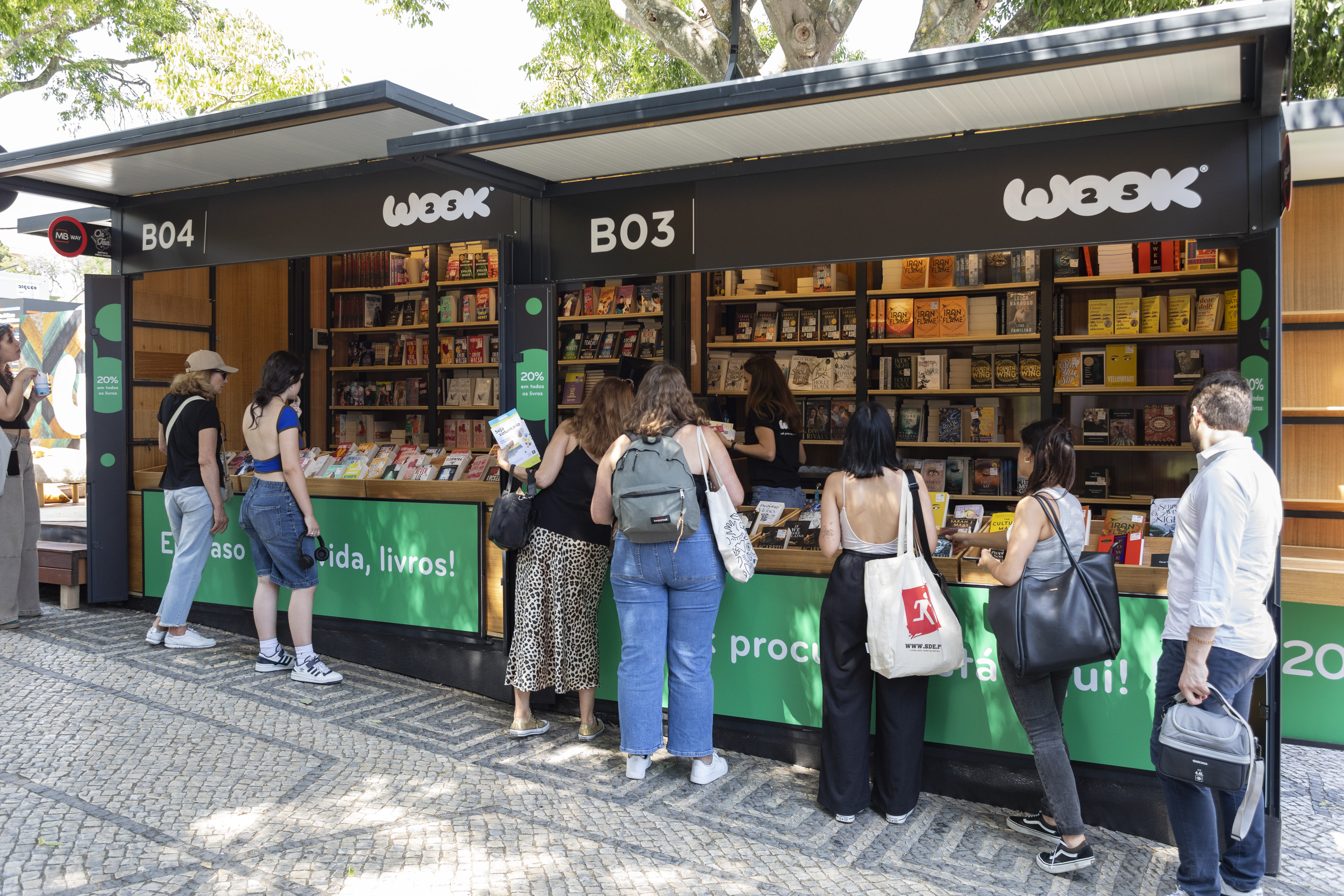 Stand da WOOK na Feira do Livro de Lisboa 2024 no Parque Eduardo VII com visitantes a explorar livros e expositores identificados B03 e B04