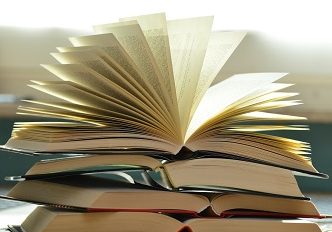 Fotografia de livro aberto com páginas abertas, visto de lado, sobre pilha de livros