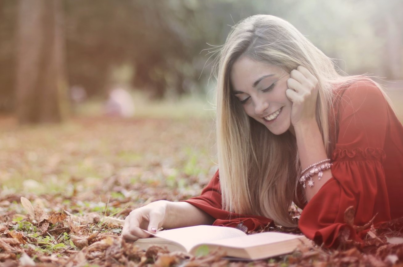 Fotografia de mulher jovem a ler deitada num jardim ao pôr do sol 